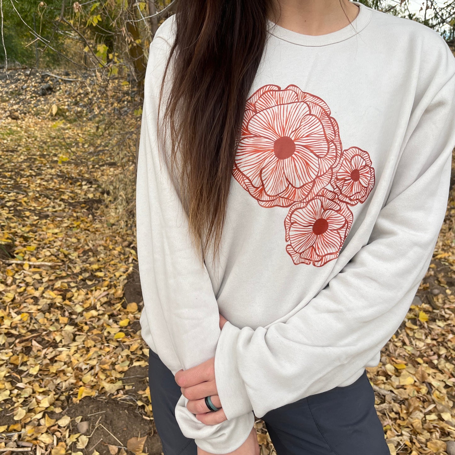 Person wearing a white sweatshirt with red floral designs outdoors on a leafy ground.