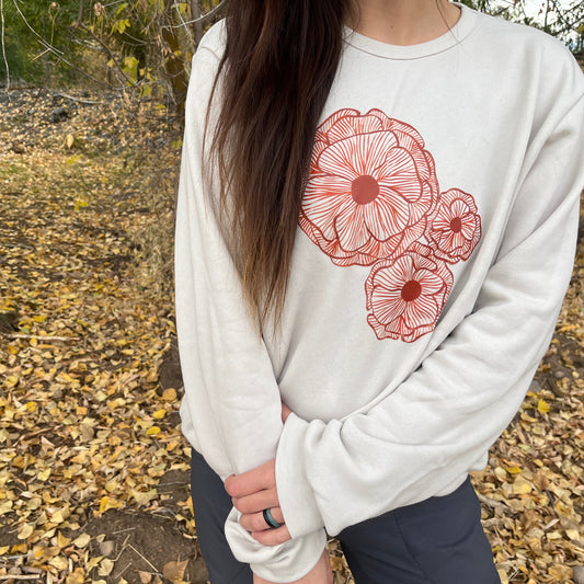 Person wearing a white sweatshirt with red floral designs outdoors on a leafy ground.